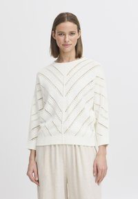 Helle Strickjacke in Creme mit einem Zickzackmuster, gerippten Bündchen und Halsausschnitt. Besitzt einen lockeren Schnitt und Dreiviertelärmel.