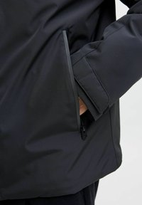 Černá, voděodolná bunda s hladkým povrchem. Obsahuje kapsu na zip a nastavitelné manžety. Minimalistický design s čistými liniemi.