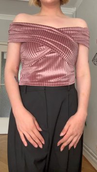 Top sin hombros en satén rosa con pliegues verticales y un diseño de frente retorcido, combinado con pantalones negros a medida.