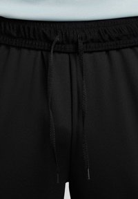 Pantalones deportivos negros con cintura elástica, que cuentan con un cordón y una textura suave. Vista en primer plano del área de la cintura.
