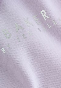 Tissus tricotés lilas avec un texte métallique argenté qui indique "BAKER BY TED BAKER." Texture douce avec un motif subtil.