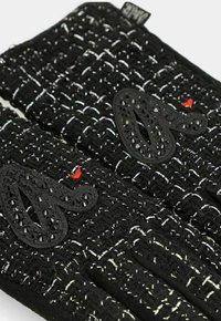 Guanti neri lavorati a maglia con fili bianchi, caratterizzati da un design testurizzato, accenti neri decorativi e un piccolo dettaglio a forma di cuore rosso.