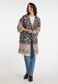 Hosszú fekete kimono, rózsaszín és zöld paisley mintával, mandzsettás ujjak és sárga díszítés. Fehér blúz és kék farmer alatt viselve.