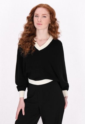 Pulover negru tricotat cu decolteu în V, dantelă de culoare crem și mâneci largi. Asortat cu pantaloni negri, având o talie ajustată.