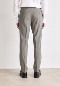 Pantaloni a quadri grigi realizzati in tessuto intrecciato, con una vestibilità dritta, due tasche posteriori con bottoni e indossati con scarpe nere.