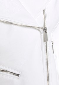 Biała kurtka z sztucznej skóry z metalowymi suwakami, teksturowaną powierzchnią, skośnym krojem i kieszeniami na zamek. Gładkie wykończenie o minimalistycznym designie.