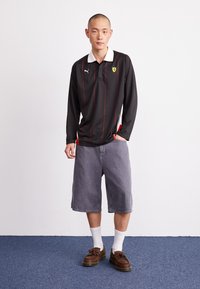 Juodas ilgomis rankovėmis polo marškinėliai su balta apykakle, raudonomis juostelėmis ir "Ferrari" logotipu; derinami su pilkais šortais ir rudos spalvos loaferiais. Matyti balti kojinės.