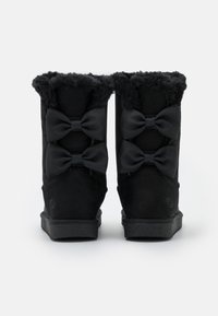 Bottines noires avec une doublure en fourrure douce, présentant trois nœuds noirs de chaque côté, fabriquées en daim avec une semelle texturée.