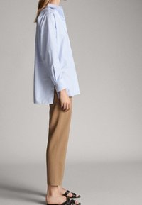 Lichtblauw gestreept shirt met een ontspannen pasvorm, verlaagde schouders en lange mouwen, gecombineerd met beige tapered broek en zwarte sandaal.