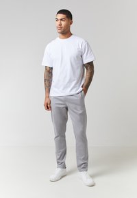 Hvit bomulls T-skjorte kombinert med lys grå bukser og hvite sneakers, med standard passform og korte ermer. Enkel design, ingen mønstre.
