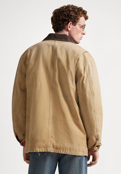 Μπεζ μπουφάν από καμβά με γιακά από κορντόρι, πλαϊνές τσέπες και μανσέτες με κουμπιά. Χαλαρή εφαρμογή με ορατές ραφές και ίσιο τελείωμα.