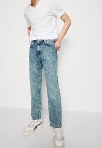 Jeans de denim de lavado claro con corte recto, combinados con una camiseta blanca de cuello en V y zapatillas blancas con acentos beiges.