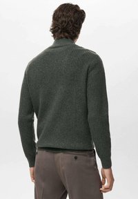 Maglione a coste verde scuro realizzato in tessuto testurizzato, con colletto alto e maniche lunghe, abbinato a pantaloni grigi.