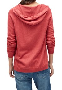 Röd hoodie med avslappnad passform, långa ärmar och snörhals, tillverkad av mjukt material med ribbade detaljer i nederkant och vid ärmsluten.