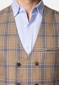 Brązowa kamizelka w kratę z niebieskimi liniami, z dekoltem w kształcie litery V, podwójnymi guzikami i kieszonką na piersi, w połączeniu z jasnoniebieską koszulą z kołnierzykiem.
