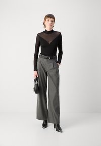 Top lungo nero trasparente con maniche lunghe, caratterizzato da un design a forma di V, abbinato a pantaloni grigi a vita alta e stivali neri con tacco.