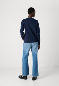Marineblå sweatshirt med rund hals og lange ærmer, parret med lyseblå vide jeans. Sorte sko med en kraftig sål. Enkel design.