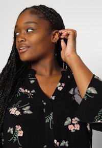 Black floral dress with green leaves and pink flowers, featuring a V-neckline and three-quarter sleeves, made from soft fabric.