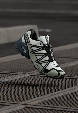 Chaussure de course légère en blanc et noir avec une tige texturée, un logo GORE-TEX et une semelle extérieure adhérente pour une meilleure traction.