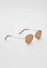 Kulaté sluneční brýle s hnědými skly a zlatým kovovým rámem. Disponují štíhlými nohami s hnědým akrylovým koncem. Minimalistický design s průhlednými nosními podložkami.