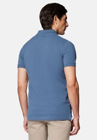 Męska koszulka polo z krótkim rękawem w jasnoniebieskim kolorze z bawełny. Posiada kołnierzyk, boczne wcięcia oraz detal z logo z tyłu kołnierza.