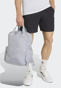 Light gray backpack with two top handles, adjustable straps, and a front pocket, featuring a subtle triangular logo on the lower front.