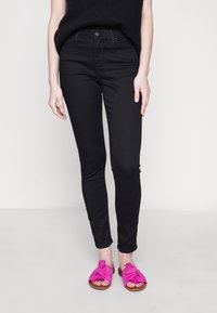 Black skinny jeans with a smooth texture, high waist, and subtle stitching details, paired with bright pink knotted slide sandals.