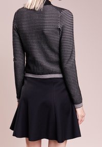 Black fitted jacket with a grid pattern and silver detailing, paired with a flared black skirt, featuring a smooth texture and elastic waistband.