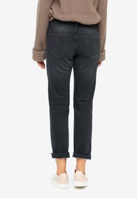 Mörkgrå jeans med en avslappnad passform, uppvikta fållar och två bakfickor, ihop med en tanfärgad stickad tröja och ljusa sneakers.