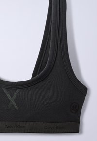 Μαύρο αθλητικό σουτιέν Calvin Klein με φαρδιές τιράντες, λεπτομέρεια σταυρωτής ραφής μπροστά και ελαστική ταινία με λογότυπο στη βάση.