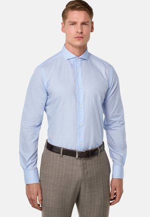 Hellblaues Langarmhemd mit feinem Streifenmuster, Button-Down-Kragen, kombiniert mit grauen Nadelstreifenhosen und einem dunkelbraunen Gürtel.