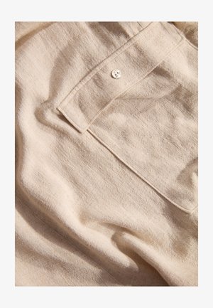 Helles beiges Gewebe mit einer strukturierten Oberfläche, ausgestattet mit einem einzigen Knopfverschluss und einer Tasche, vermittelt das Aussehen von natürlichem Leinen.