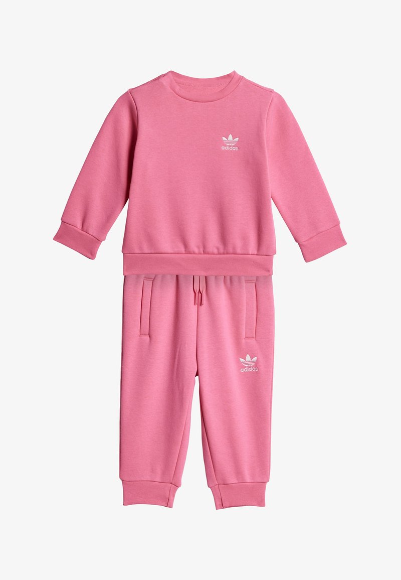 Conjunto de sudadera y pantalones adidas en rosa, fabricado con tejido suave. Presenta puños acanalados, bolsillos laterales y un logo blanco en ambas piezas.