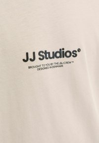 Nahaufnahme von beigem Stoff mit schwarzem Text, auf dem steht: 'JJ Studios, präsentiert von der J&J Crew, entworfen in Dänemark'.