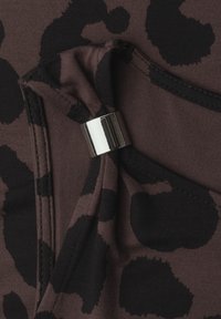 Tissu marron foncé avec de grandes taches noires irrégulières, rassemblé et maintenu avec un accessoire anneau rectangulaire argenté brillant.