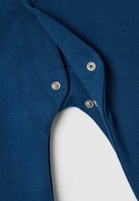 Abito in cotone blu con chiusure a scatto, caratterizzato da una consistenza morbida e un design aderente. Dettaglio di tessuto sovrapposto sul collo e sulle aperture delle gambe.