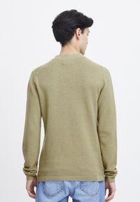 Pulover texturat de culoare verde măsliniu, cu guler rotund, mâneci lungi și manșete cu nervuri. Purtați-l cu blugi din denim de culoare bleu deschis.
