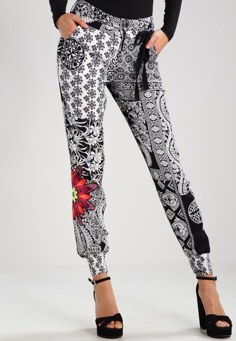 Femme portant un pantalon noir et blanc taille haute avec un motif de fleur rouge sur la jambe et des sandales à talons noires.