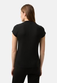 Černé tričko s krátkým rukávem z hladké látky, s kulatým výstřihem a viditelnými švy na zádech, nošené s černými kalhotami.