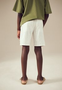 T-shirt vert surdimensionné, short blanc à rayures, sandales marron clair avec détail nœud. Tissu doux, design décontracté, short mi-cuisse.