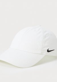 Biała czapka bejsbolowa wykonana z bawełny, z zaokrąglonym daszkiem. Posiada małe czarne logo Nike po lewej stronie. Prosty, nieozdobiony design.