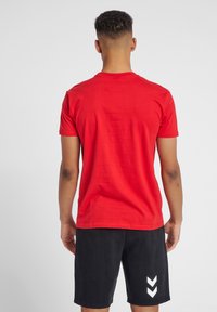 Rood t-shirt met korte mouwen van katoen. Heeft een ronde hals en een gladde textuur. Gecombineerd met zwarte shorts met witte chevronaccenten.
