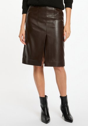 Gonna in pelle marrone al ginocchio con spacchi frontali, dotata di due tasche frontali e una superficie liscia e lucida. Stivaletti neri alla caviglia completano l'outfit.