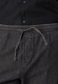 Pantalons noirs, doux et extensibles avec une taille élastique et un cordon de serrage. Présentent une texture subtile et des poches latérales.