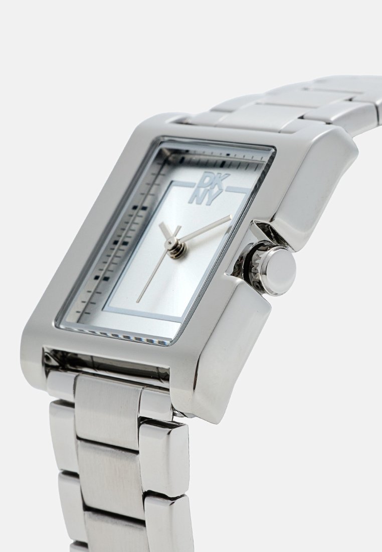 Montre rectangulaire argentée avec un bracelet en acier inoxydable, cadran minimaliste avec un fond bleu clair, et une couronne pour le réglage de l'heure.