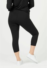 Black three-quarter length leggings made of a smooth, stretchy material, paired with white sneakers. Simple design with no visible patterns.