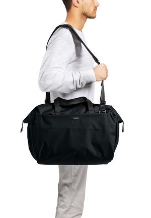 Borsa da viaggio nera in tessuto strutturato, dotata di doppi manici e tracolla regolabile. Logo visibile sulla parte anteriore.