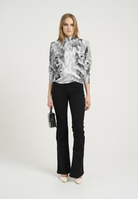 Top a maniche lunghe grigio e bianco con un alto colletto, abbinato a pantaloni neri a zampa d'elefante e tacchi bianchi a punta, mentre tiene una pochette nera.
