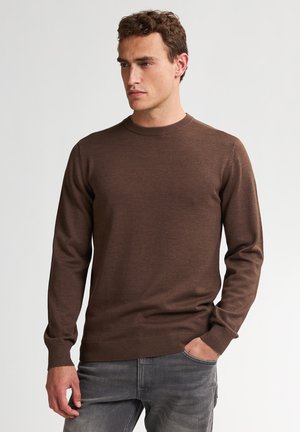 Suéter marrón de manga larga y cuello redondo, hecho de un tejido de punto suave. Los puños y el dobladillo acanalados añaden textura. Combinado con vaqueros grises.