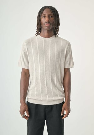 Knit short-sleeve sweater in light beige with a ribbed texture and vertical stripes. Paired with black pants. No notable hardware.